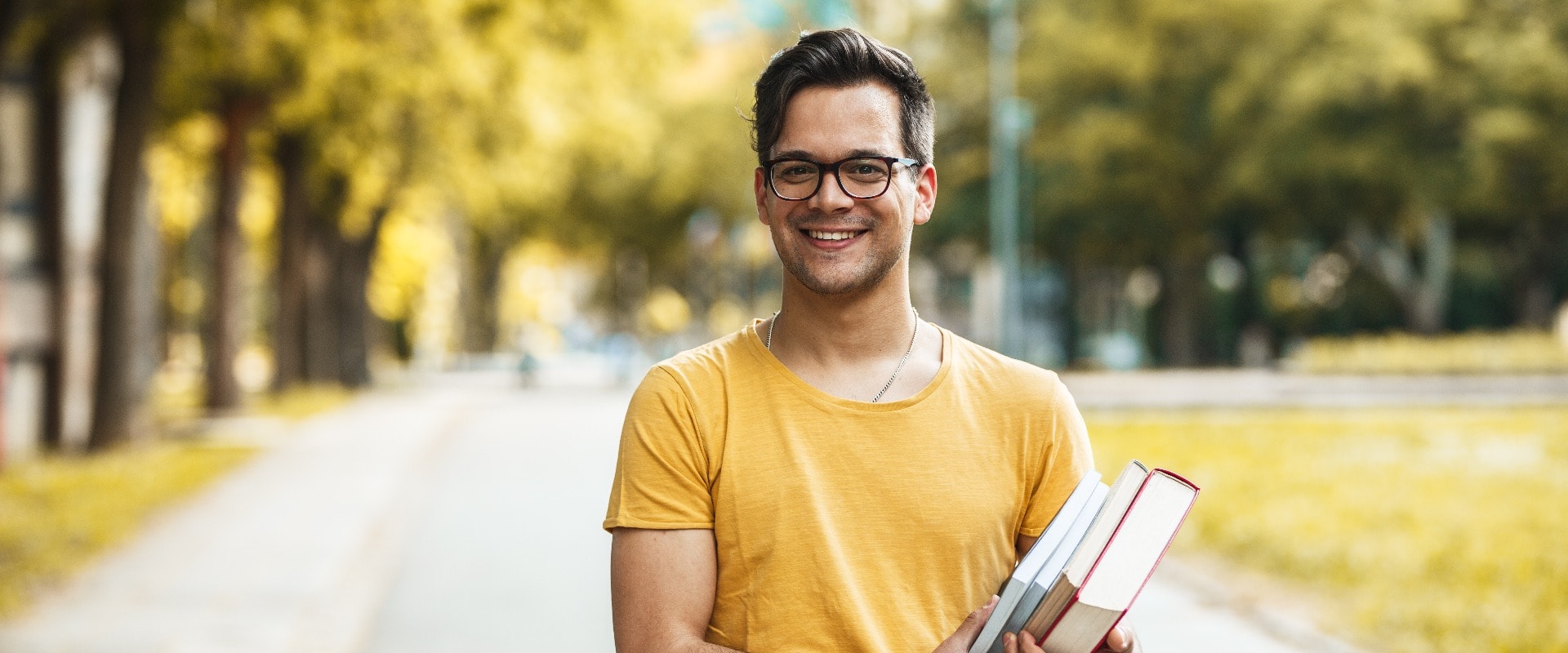 Young male student standing at the college yard.He holding a book and looking at camera.